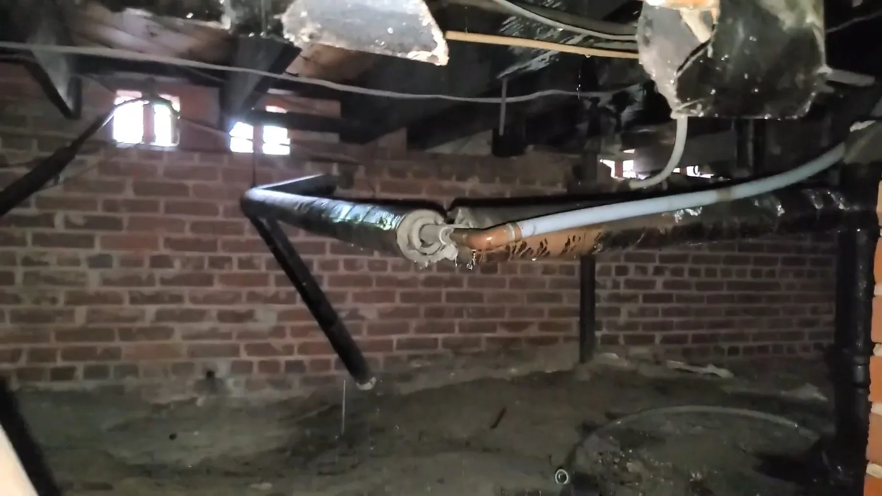 Old plumbing exposed below a crawlspace access point