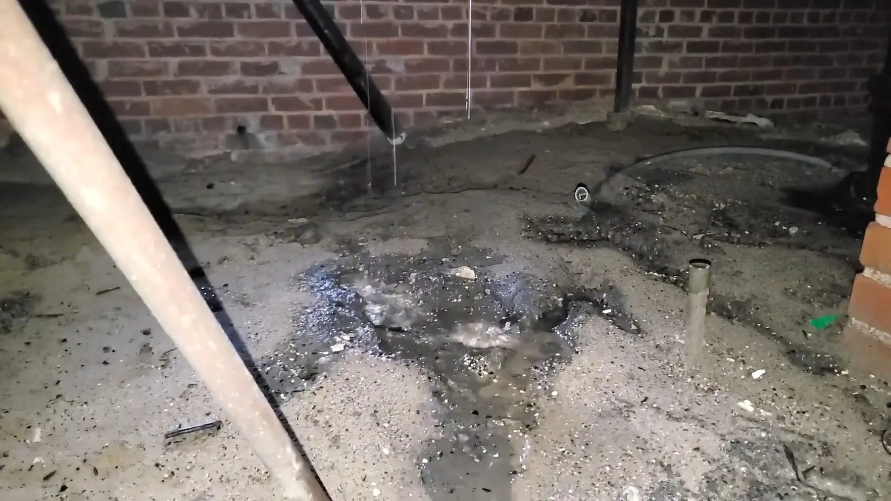 Wet ground beneath a leaking crawlspace pipe, saturating the soil below the floor